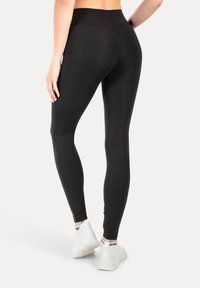 Leggings negros de cintura alta con una textura suave y un diseño ajustado, combinados con zapatillas deportivas blancas que exhiben un logo en el talón.