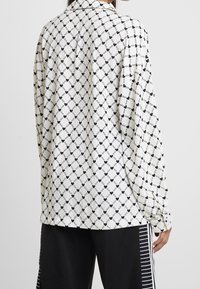 Camicia a maniche lunghe in tessuto bianco con un motivo a rombi neri, caratterizzata da cuori e catene. Vestibilità rilassata, polsini con bottone e colletto classico.