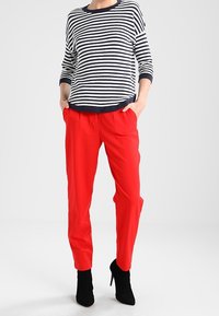 Gestreifter marineblau-weißer Pullover mit 3/4-Ärmeln, kombiniert mit leuchtend roten Hosen. Schwarze High-Heel Stiefeletten runden das Outfit ab.