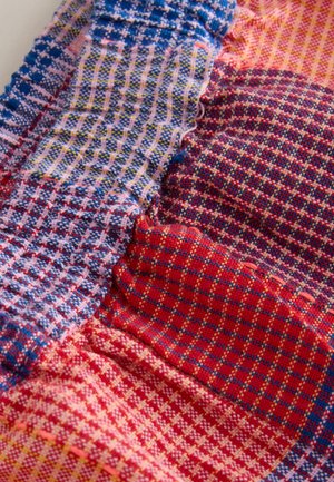 Lappetæppe med forskellige ternede og rutede stofstykker i røde, blå, gule og lyserøde nuancer syet sammen.