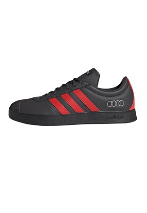 Zapatillas sintéticas negras con rayas rojas y logotipo gris de Audi, con suela de goma y diseño de punta redondeada.