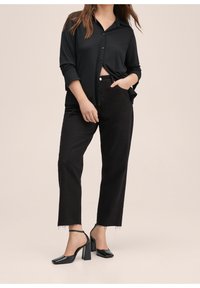 Camisa negra de botones con mangas arremangadas, combinada con jeans negros de cintura alta. Zapatos negros de tacón cuadrado con una correa en el tobillo.