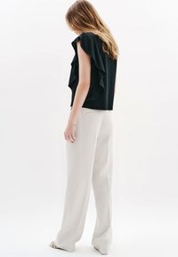 Svart topp med volangärmar som kombineras med ljusbeige vida byxor. Toppen har lager av volanger, medan byxorna har en slät textur och skräddarsydd passform.