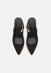 Chaussures slingback à bout pointu noires avec une finition en tissu lisse, présentant un design découpé sur les côtés et un talon ouvert pour un look moderne.
