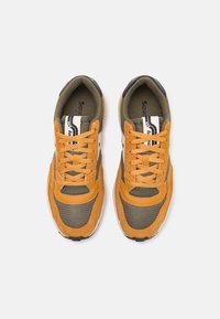 Oransje og olivengrønne joggesko laget av semsket skinn og mesh, med svarte detaljer, rund tå og kontrasterende lisser.