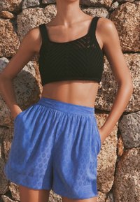 Haut court en maille noire avec un motif géométrique, associé à un short ample bleu clair avec un design embossé subtil. Tissu texturé et respirant.