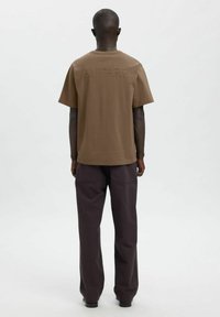 Pruun puuvillane t-särk, millel on seljal tikandiga "ANNARR", koos tumelilla laiade pükstega. Lihtne, lõdvestunud istuvusega disain.