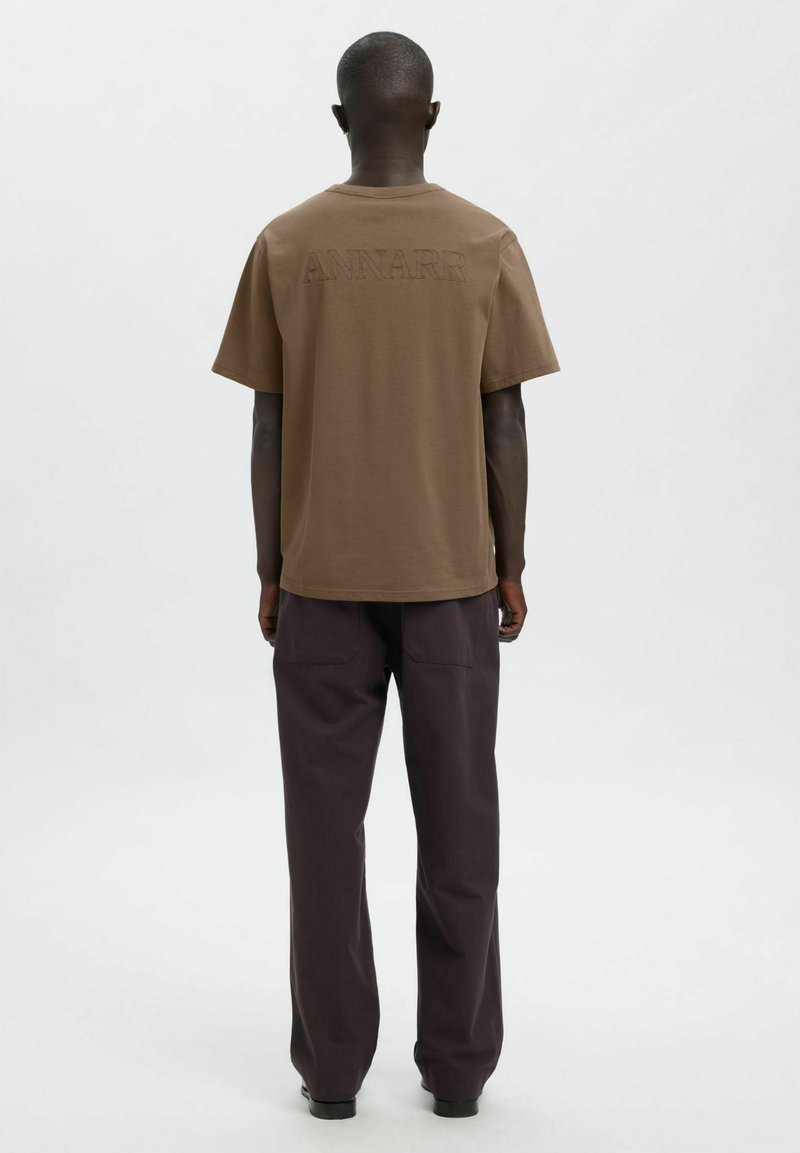 Pruun puuvillane t-särk, millel on seljal tikandiga "ANNARR", koos tumelilla laiade pükstega. Lihtne, lõdvestunud istuvusega disain.