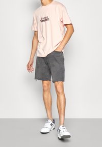 Camiseta de algodón rosa con el texto "Corriendo de manera más inteligente", combinada con shorts de denim grises con dobladillos deshilachados y zapatillas blancas con detalles grises.