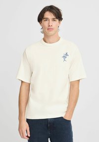 Cremefarvet kortærmet t-shirt lavet af bomuld, med blå blomsterbroderi på venstre bryst, rund halsudskæring og afslappet pasform.