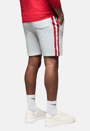 Grå svedshorts med to røde sidelister, elastisk talje og baglomme. Sammen med hvide sneakers og hvide sokker.