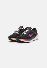 Zapatillas deportivas negras con parte superior de malla, acentos morados, cordones blancos y una entresuela en degradado de naranja y rosa. Presentan una superficie texturizada y un logo.