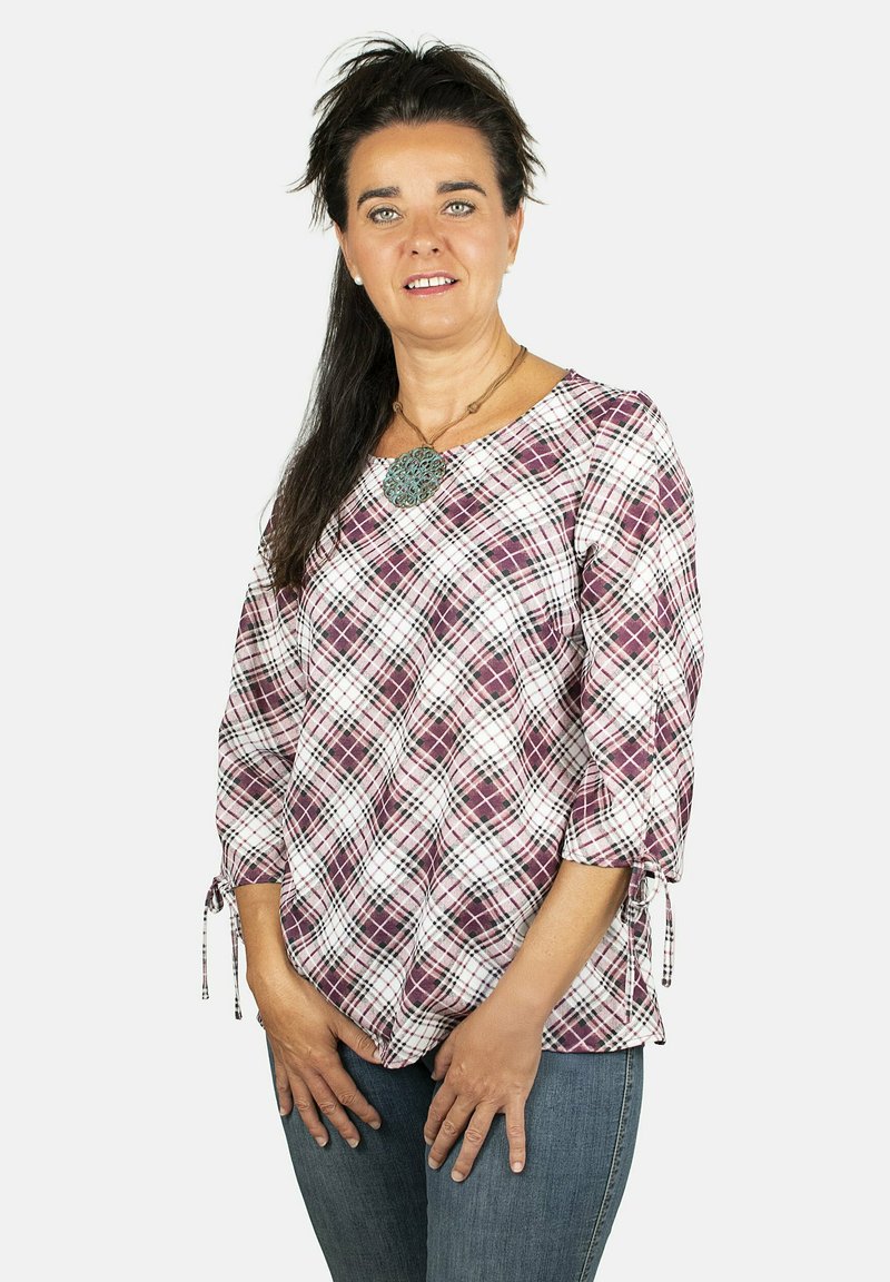Blusa de corte suelto de cuadros en blanco, morado y rosa, con mangas de tres cuartos y detalles de lazo en los puños. Textura de tela suave.