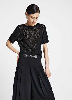 Top nero lavorato a maglia con motivo geometrico a traforo, maniche corte e scollo arrotondato, abbinato a pantaloni neri plissettati con cintura.