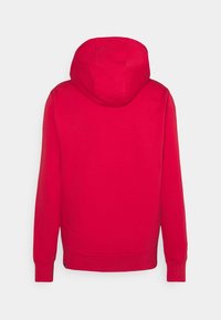 Sweat à capuche rouge vu de dos avec manches longues et poignets et bas côtelés sur un fond clair uni.