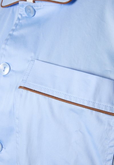 Γαλάζιο πουκάμισο με τσέπη με καφέ περίγραμμα και κουμπιά στο ίδιο χρώμα σε λείο ύφασμα.