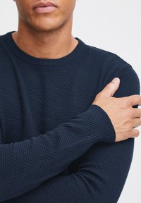 Marineblauer Strickpullover mit strukturiertem Muster, rundem Ausschnitt und gerippten Bündchen. Der Stoff wirkt weich und atmungsaktiv.