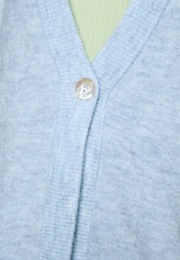 Svetle modrý kardigan z měkké pleteniny má výstřih do V a na přední straně světle zbarvený knoflík z matného perleti.