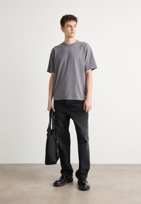 T-shirt en coton gris avec une coupe décontractée, manches courtes. Assortie à un pantalon en denim noir, des chaussures noires et un sac noir. Design simple, détails minimaux.