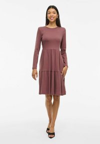 Långärmad mauve klänning med en figursydd överdel, ett fläktande kjol och mjuk ribbad textur. Har rund halsringning och längd till mitten av vaden.