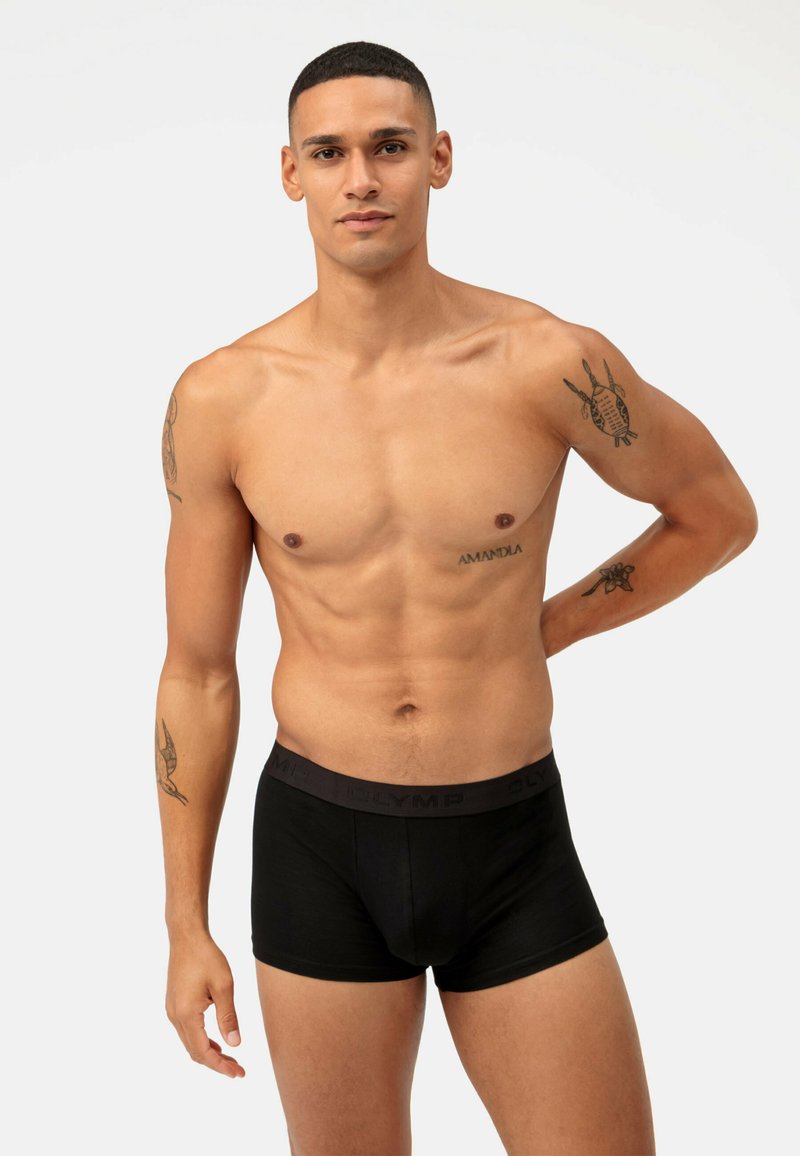 Boxer da uomo neri in tessuto morbido con una texture liscia. Presenta un cinturino scuro con il logo "OLYMP". L'uomo è in piedi con le braccia rilassate.