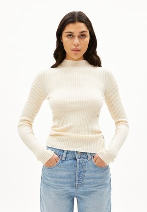 Crème kleurige geribde trui met een hoge hals en lange mouwen, gecombineerd met lichtblauwe high-waisted jeans met voorzakken.