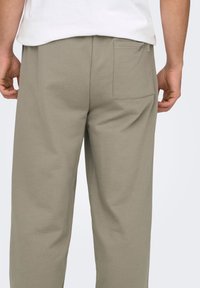 Pantalon coupe décontractée en mélange de coton de couleur vert olive atténué. Il dispose d'une poche arrière et d'une texture douce et lisse avec une coupe droite.