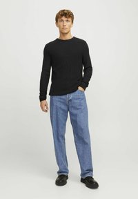 Black ribbed long-sleeve shirt paired with loose light blue jeans and black footwear, set against a plain light background.