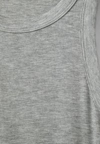 Szürke bordázott ujjatlan felső, kerek nyakkivágással és puha tapintással. Az anyag szolid színváltozásokat és szoros vízszintes vonalakat mutat.