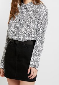 Vit blus med svart djurtryck, knäppt fram, långa ärmar. Kombination med svart denim minikjol och svart bälte.
