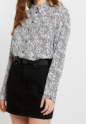 Blusa bianca con stampa animale nera, con bottoni, maniche lunghe. Abbinata a una mini gonna in denim nera e a una cintura nera.
