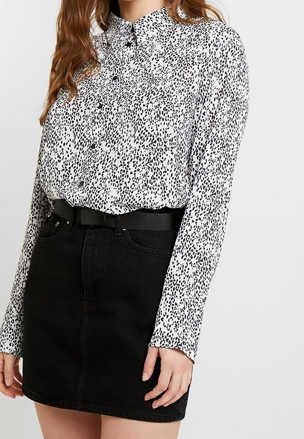 Vit blus med svart djurtryck, knäppt fram, långa ärmar. Kombination med svart denim minikjol och svart bälte.