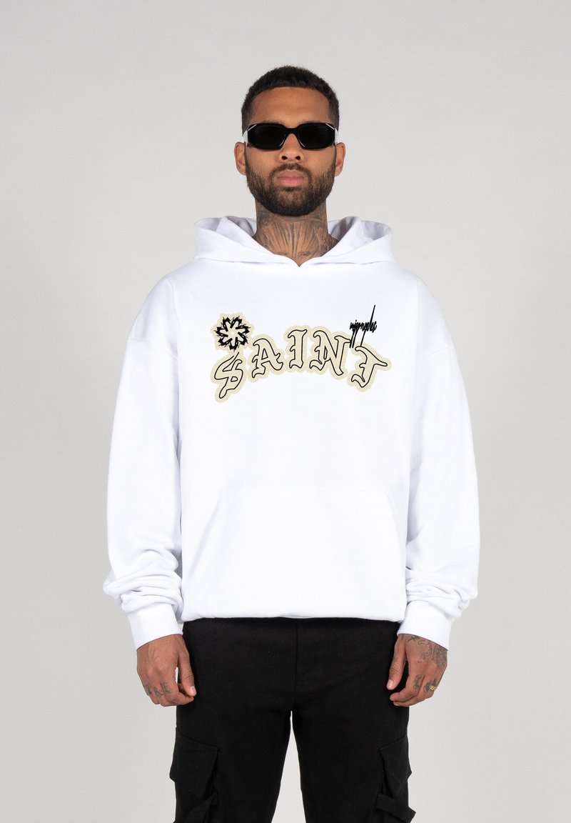 Witte hoodie met geborduurd "SAINT" in goud en zwart. Heeft een frontzak en een capuchon met trekkoord. G gedragen met zwarte cargo shorts.