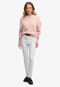 Pull tricoté rose clair à col rond, associé à un jean blanc à coupe slim et des chaussures noires à lacets. Texture subtile sur le pull.