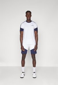 Witte en marineblauwe sportt-shirt met korte mouwen, gecombineerd met shorts met marineblauwe accenten. Inclusief logodetail op de borst. Klassieke pasvorm.