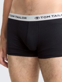 Primo piano di una persona che indossa boxer neri Tom Tailor con un elastico bianco e peli visibili sulle gambe e sull'addome inferiore.