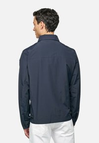 Giacca blu navy realizzata in tessuto leggero, con colletto, maniche lunghe e dettagli a bottoni sui polsini e sull'orlo.