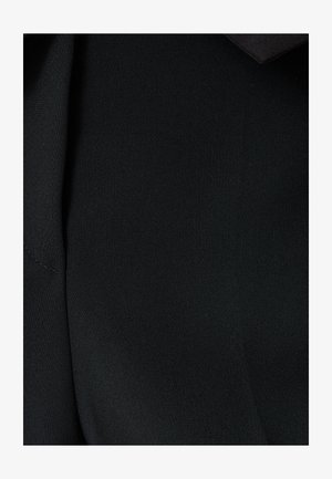 Mustan kankaan lähikuva, sileä rakenne, jossa on lievä kiilto. Sisältää sauman ja taitetun muotoiluelementin.