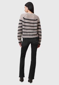 Maglione a righe in beige e nero, caratterizzato da una vestibilità ampia, un tessuto texturizzato e un collo rotondo, abbinato a jeans neri a zampa.