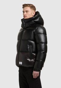 Black puffer jacket with a glossy finish, featuring a high collar, zip closure, and large quilted sections. Logo tag on the lower edge.