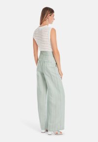 Weißes Häkeloberteil mit ärmellosem Design, kombiniert mit hochtaillierten, hellgrün gestreiften, weit geschnittenen Hosen. Auffällige offenmaschige Textur.