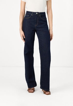 Jeans en denim noir taille haute avec une jambe droite, des coutures contrastantes et des poches avant, assortis à des sandales à talons marron.