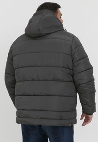 Gray puffer jacket with a hood, featuring quilted sections and a smooth, shiny texture. Includes a brown accent tag on the bottom.