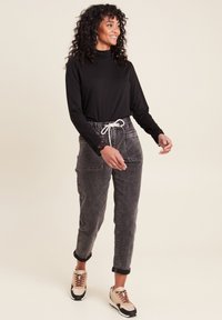 Zwarte lange mouw top met een hoge hals, gecombineerd met grijze denim broek met opgestikte zakken en een witte trekkoord. Beige en zwarte sneakers.