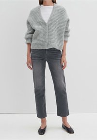 Cárdigan gris de punto con escote en V y tres botones, combinado con vaqueros grises y mocasines negros. Textura suave, corte relajado y longitud corta.