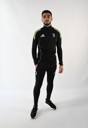 Chándal deportivo negro con parte superior de media cremallera, con acentos en amarillo y rosa, y leggings negros. Logo de Adidas y escudo de la Juventus visibles.
