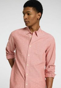 Camisa de botones rosa claro hecha de tejido texturizado, con cuello, mangas largas enrolladas en los puños y pequeños botones blancos.