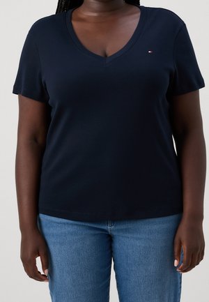 Navy blue cotton t-shirt with a V-neck, short sleeves, and a small logo on the chest. Worn with light blue denim jeans.