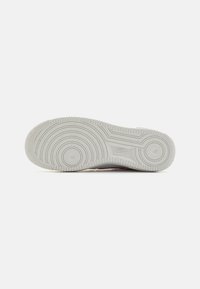 Suola di sneaker Nike in gomma grigia chiara, con motivi di trazione circolari e una superficie testurizzata, con dettagli spruzzati.