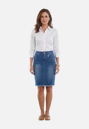 Donna in piedi di fronte, indossa una camicia bianca a maniche lunghe con bottoni, una gonna di jeans fino al ginocchio e mocassini marroni su sfondo bianco.